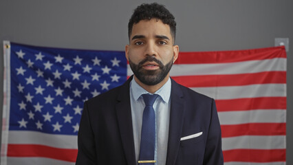 Handsome hispanic man in suit stands before american flag, suggesting political or electoral context.