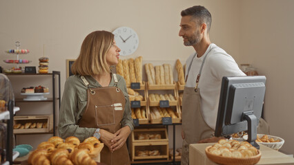 Man and woman in aprons talking inside a bakery shop with shelves of bread in the background