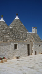 Traditional trulli house in alberobello, italy with conical roofs, white stone walls, and a vivid blue sky in the background.