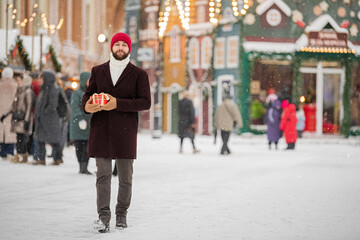 Happy smiling man in winter clothes at street Christmas market walking with gifts in hands.