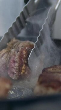 turn the steak cook steak in a frying pan. Grilling Delicious Tender Cut of Alberta Beef Steaks on a BBQ Grill. Summer Barbecue Cookout Weekend Party and Flipping or Turning Meat with Tongs