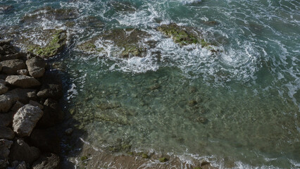 Calm, clear seawater splashes over rocks on the coastline of gallipoli, puglia, salento, italy, featuring a peaceful natural shoreline with waves and algae.