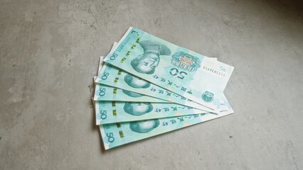 Chinese banknotes arranged on concrete surface display various fifty-yuan bills, emphasizing...