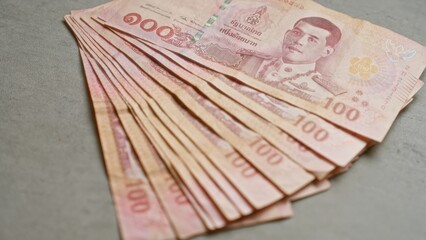 Thai banknotes in various amounts are displayed on a concrete surface, highlighting the distinct design and currency of thailand's baht.