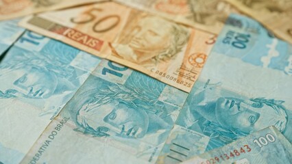 Brazilian banknotes scattered, featuring 10, 50, and 100 reais denominations, representing brazil's currency and financial concept.