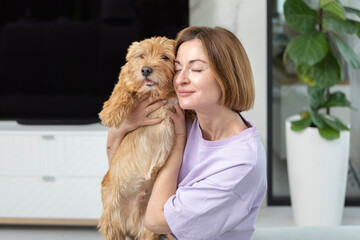 Young and beautiful woman sitting on the couch and hugging her adorable pet dog. Perfect friendship concept	