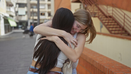 Two women embracing happily on a city street, showcasing friendship in an urban outdoor setting.