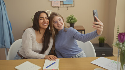 Two women friends taking selfie at home with smartphone, showing happiness and companionship in a cozy apartment.