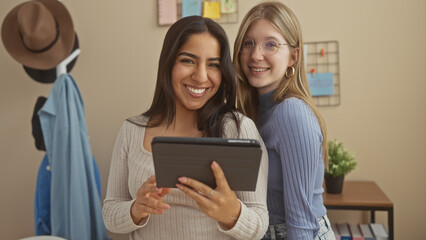 Two smiling women friends sharing a tablet in a cozy living room setting.