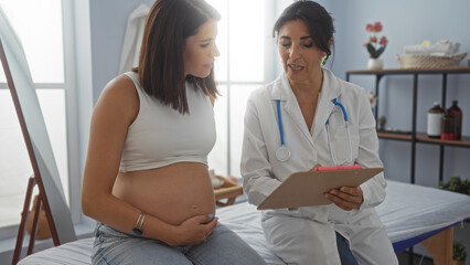 Fototapeta premium Pregnant woman consulting female doctor in a clinic room discussing pregnancy and medical care.
