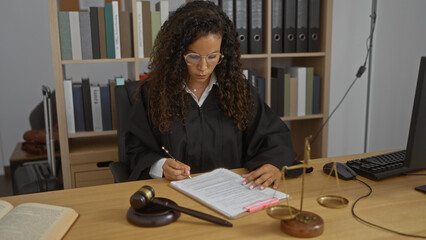 Woman judge with curly hair and glasses working in office, signing legal documents at desk with...