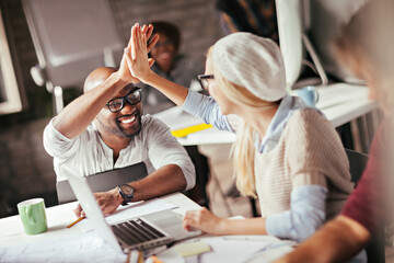 Diverse young designers high fiving in modern office