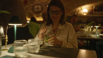 A young hispanic woman enjoying a drink in an indoor italian restaurant, surrounded by a cozy ambiance with dim lighting and a relaxed atmosphere.