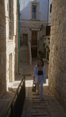 A young, beautiful, hispanic woman walks the historic stone streets of polignano a mare, puglia, italy, basking in the charming european architecture.