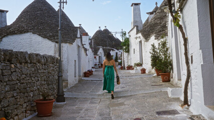 A young hispanic woman in a green dress walks through the picturesque old town of alberobello,...