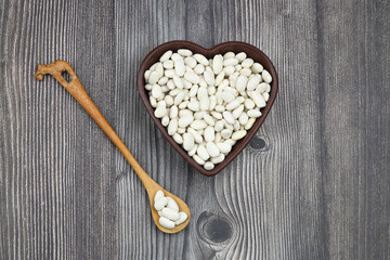white kidney beans in a heart shaped bowl a on wooden background.Top view.