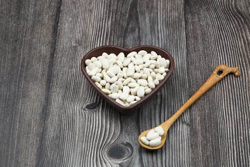 white kidney beans in a heart shaped bowl a on wooden background.Top view.