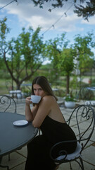 A beautiful young woman enjoying a cup of coffee outdoors in a charming villa garden in puglia, italy, surrounded by lush greenery and tranquil scenery.