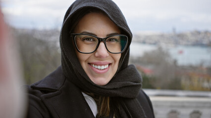 Smiling woman with glasses taking a selfie in istanbul with scenic cityscape background.