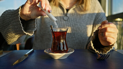 A woman sweetening her tea at an outdoor cafe with modern attire, capturing a relaxed urban...