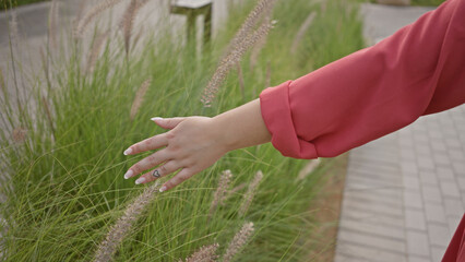 Elegant woman in red touches tall grass in a serene park setting, symbolizing tranquility and connection with nature.
