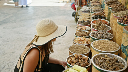 A young woman in a straw hat explores a traditional market in dubai, surrounded by colorful spices...