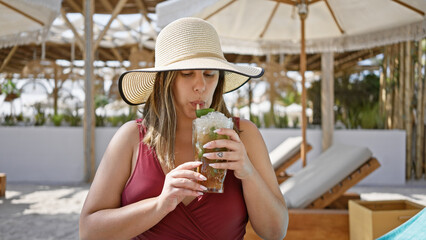 A young woman in a sunhat sipping a mojito at a luxurious beach resort.