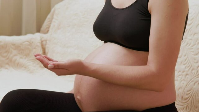 Close-up image of a pregnant woman with a beautiful belly takes out moisturizing oil from a container, gently massaging her belly to prevent stretch marks during pregnancy. Self care during pregnancy