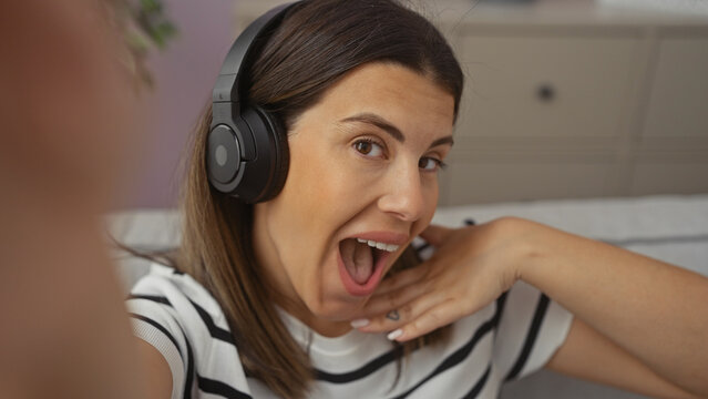 A joyful woman with headphones taking a selfie in a modern apartment living room.