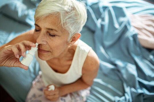 Senior woman using nasal spray on bed at home