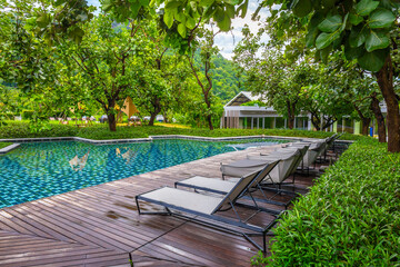 large swimming pool with poolside chair in a garden surrounded by trees besides the hotel.