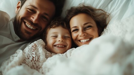 A family of three, including a smiling child, lies closely together under a soft white blanket, capturing a moment of togetherness, warmth, and genuine happiness in a cozy setting.