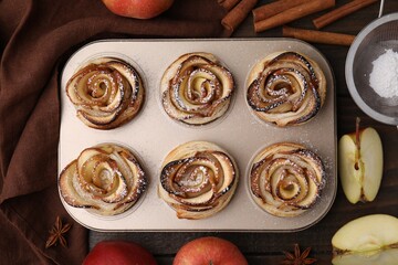 Freshly baked apple roses and ingredients on wooden table, flat lay. Puff pastry