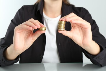 Financial inequality. Woman comparing two stacks of coins at table, closeup