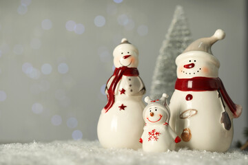 Cute decorative snowmen on artificial snow against blurred lights. Space for text