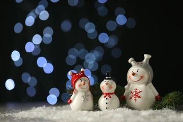 Cute decorative snowmen and fir branches on artificial snow against blurred lights. Space for text