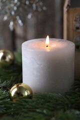 Burning candle, baubles and fir branches on blurred background, closeup. Christmas atmosphere
