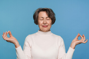 Beautiful calm mature woman close eyes smiling feels good folded fingers mudra gesture makes yoga...