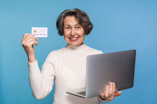 Portrait of cheerful smiling satisfied retired mature woman hold laptop netbook demonstrate credit card ecommerce doing online shopping order delivery booking tour isolated on blue color background