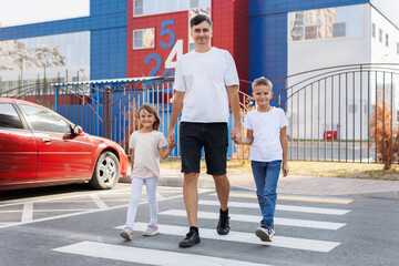 A father with his son and daughter cross the road at a pedestrian crossing.