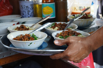 Tukang Mie Ayam or a noodle vendor preparing servings of chicken noodle soup.