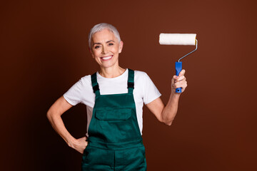 Photo of cheerful lovely senior specialist woman wear green workwear hold brush isolated on brown...