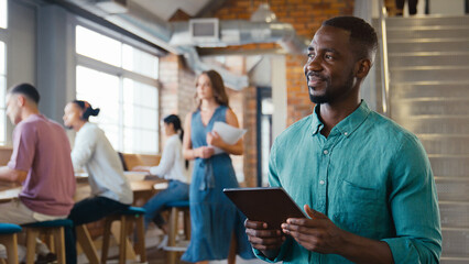 Smiling Businessman Using Digital Tablet Working In Busy Modern Open Plan Office 