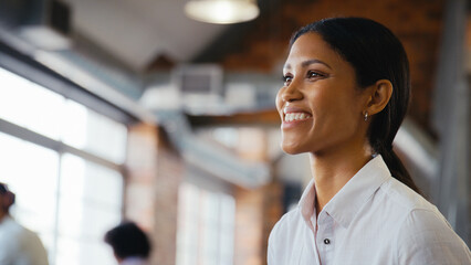 Close Up Of Smiling Young Businesswoman Working In Open Plan Office With Colleagues In Background