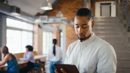 Businessman Using Digital Tablet And Stylus Pen Working In Office With Colleagues In Background 