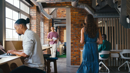 Busy Multi-Cultural Open Plan Office With Businesspeople Working At Desks And Meeting Colleagues