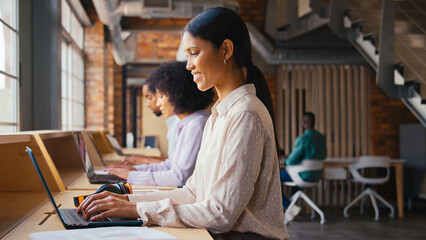 Businesswoman With Laptop Working In Busy Modern Multi-Cultural Open Plan Office With Headphones