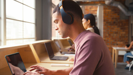 Businessman Working In Busy Modern Multi-Cultural Office Listening To Music On Wireless Headphones