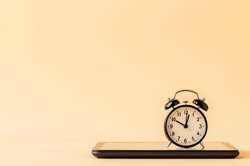 An analog alarm clock stands on a digital tablet, symbolizing screen time management.