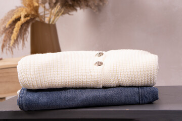  A folded cream knit sweater placed on top of folded denim jeans, styled with minimalistic decor, with copy space.